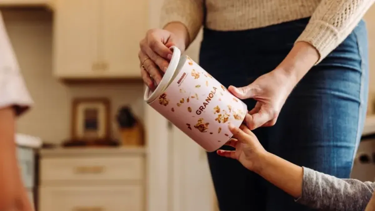 A person's hands are seen holding a paper container labeled "granola."