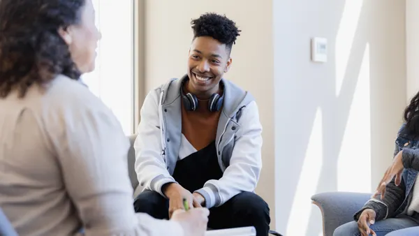 A teen is smiling while listening to his mentor encourage him.