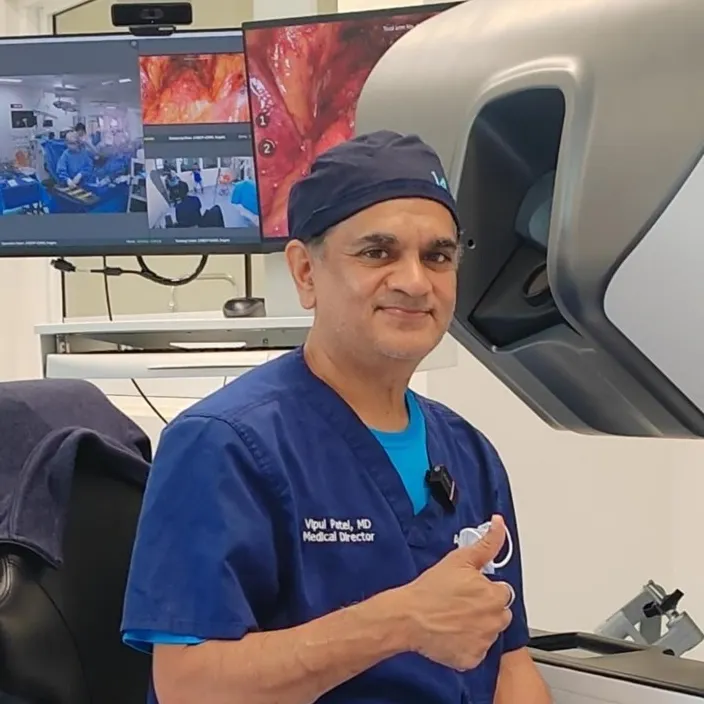 A surgeon seated at a robotic system console gives the thumb's up.