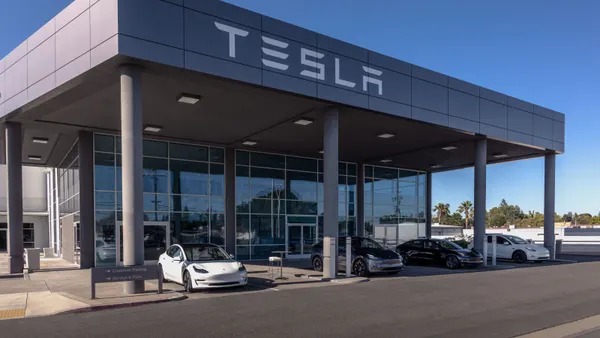 Electric vehicles parked outside a Tesla store with the named "Tesla" spelled out on the side of the building.