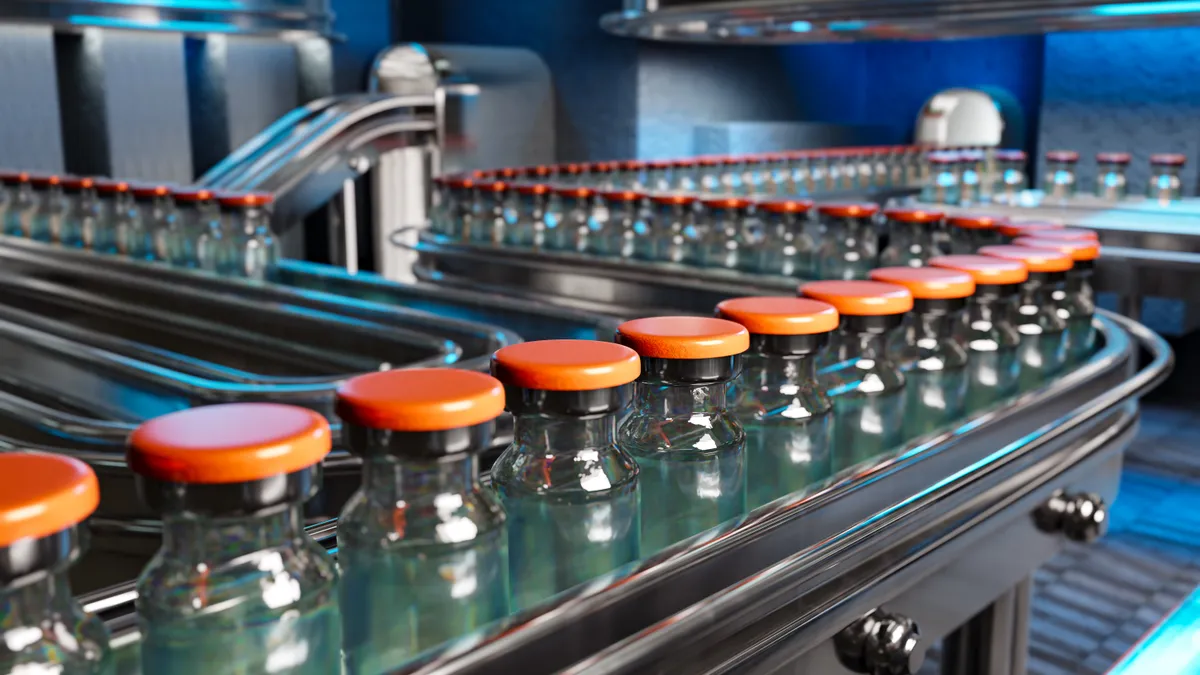 Glass vials with orange caps sit on a pharmaceutical factory production line.