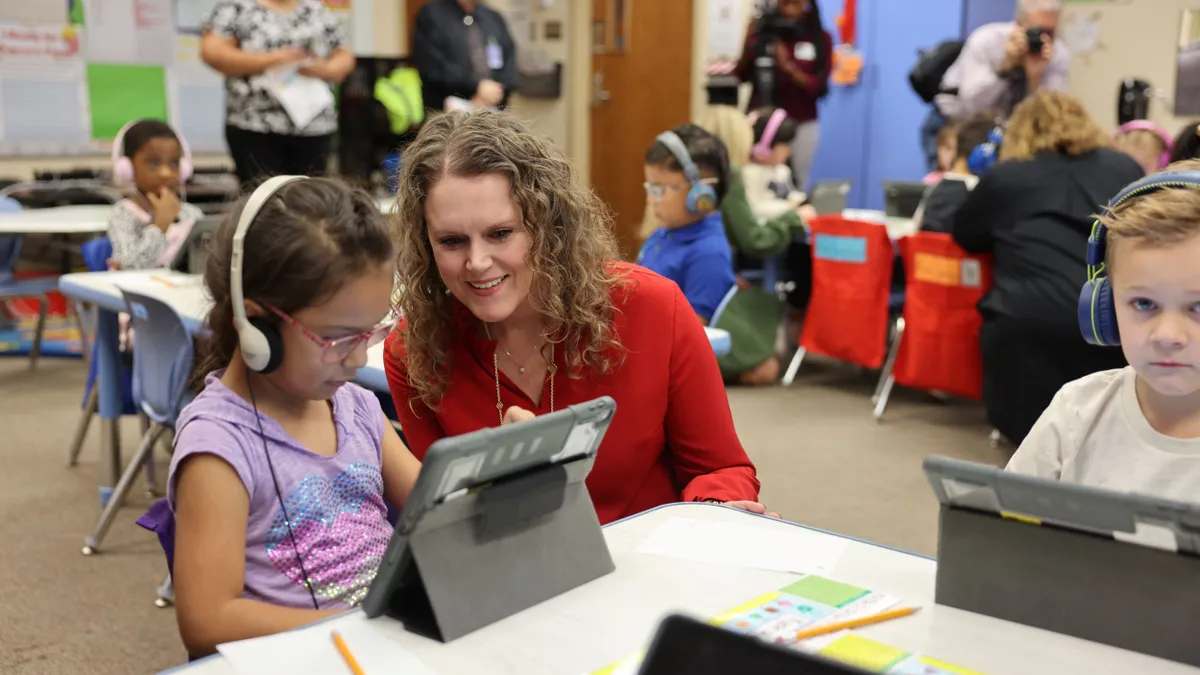 A young student wears headphones while using a tablet device as Ector County ISD’s superintendent watches from the student’s right.