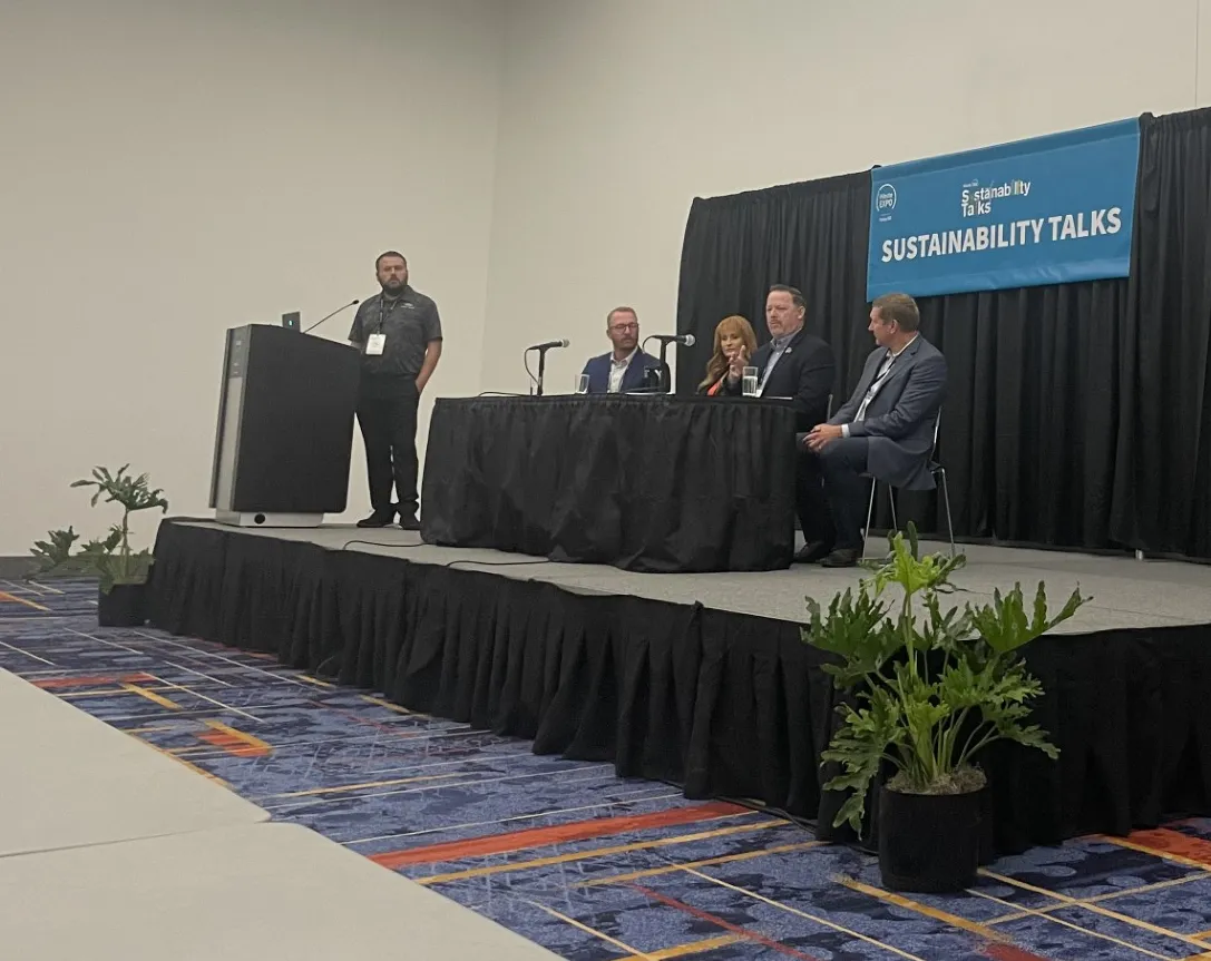 One person stands, with four people seated at a table, on stage at WasteExpo 2024