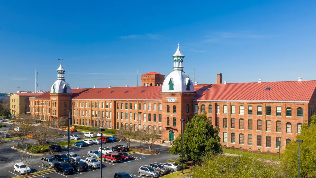 Three-story brick building with trees and cars in the foreground.