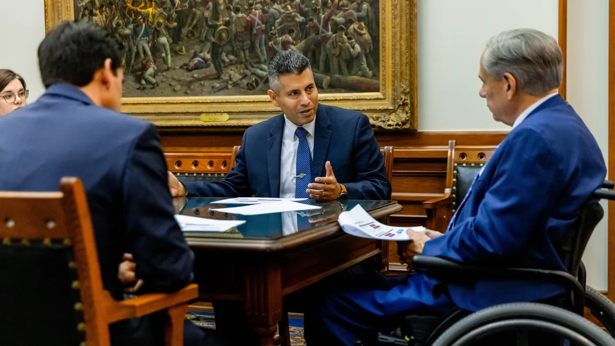 Entergy Texas President and CEO Eliecer Viamontes sits at a table with Texas Gov. Greg Abbott, discussing the utility's plan to build two new power plants.