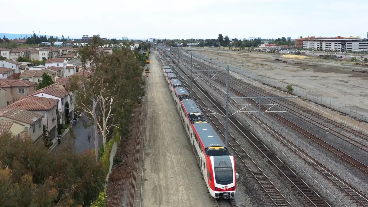 A train rides along on a track, red and white. An overhead camera captures the movement.