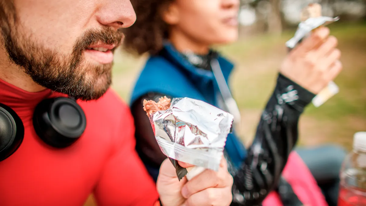 Two people sit and eat granola bars