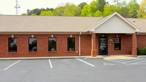 A view of a one-story brick building with a glass door entrance along with part of a parking lot.