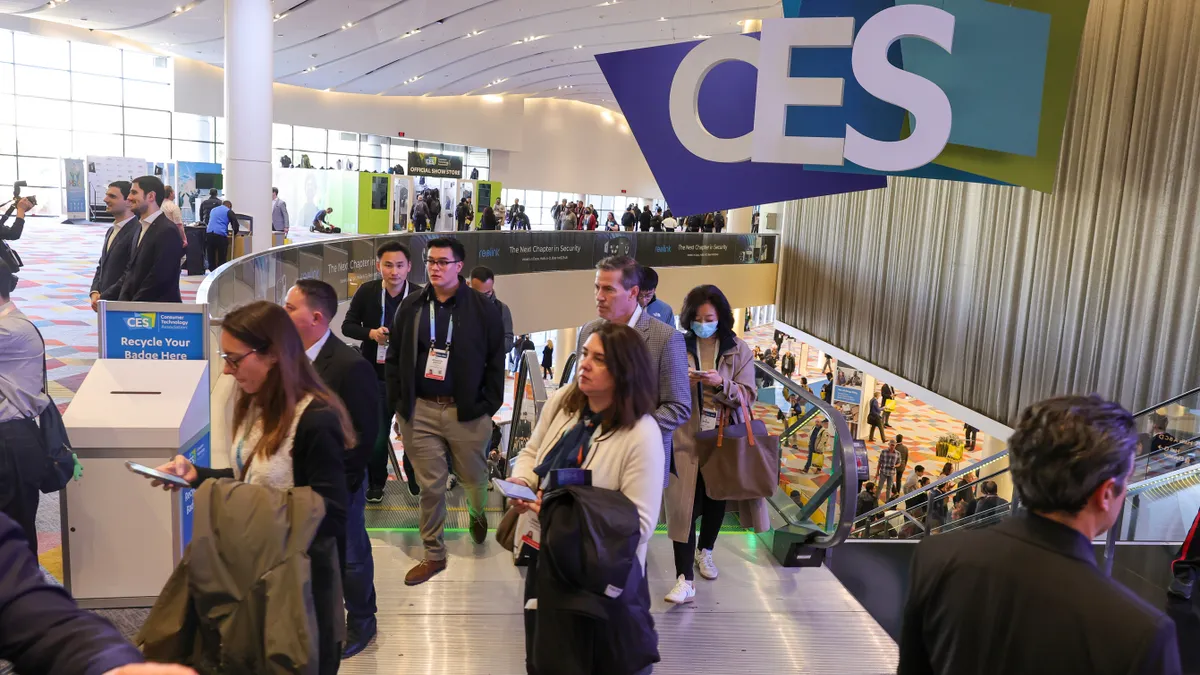 A group of people in a hotel pass under a CES sign. The people are dressed in either casual, business-casual, or business clothes.