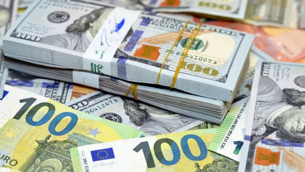 Stacks of U.S. 100 dollar bills piled atop European banknotes, including Euros.
