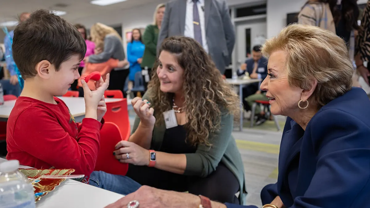 Two adults kneel down to talk with a student seated in a chair