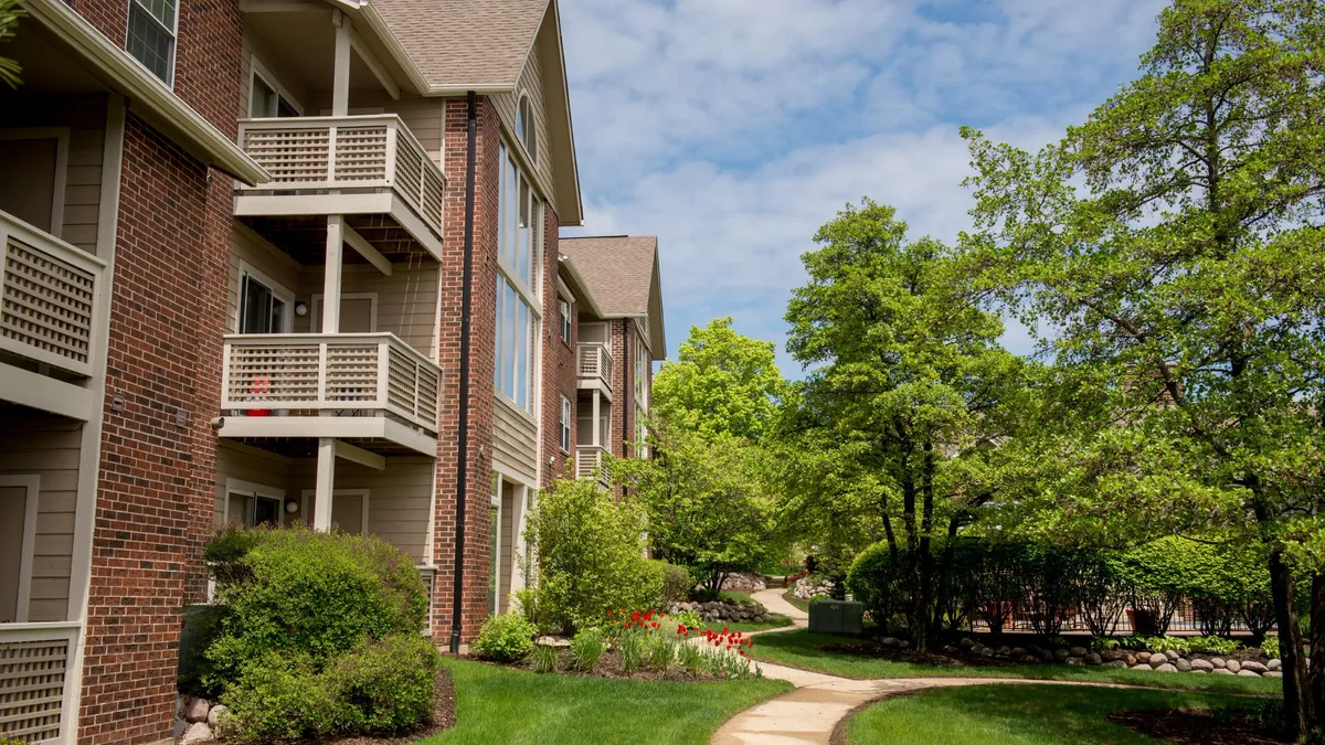 Brown three-story apartments on the left and trees on the right.