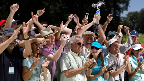 A cheering crowd of fans stands at the rope at a golf course.