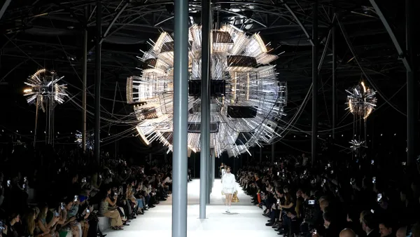 Models walk the runway beneath an elaborate light fixture.