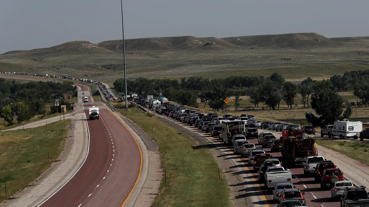 Car traffic lines up on a highway with rolling hills in the background