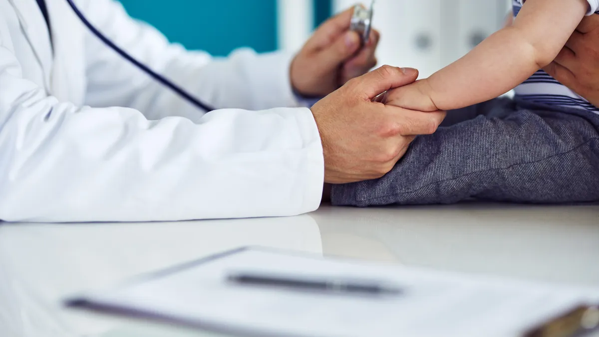Doctor seeing young patient, holding their hand and a stethoscope.