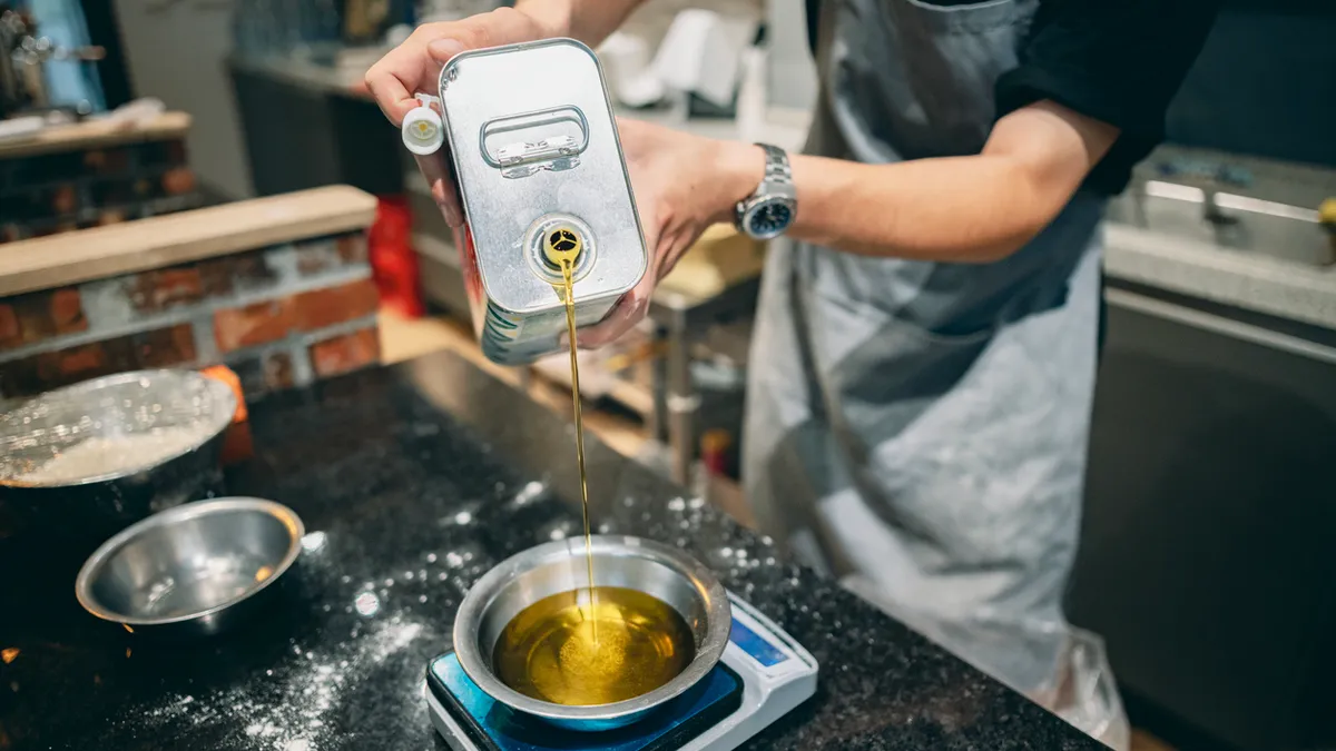 Male in apron pouring oil from canister