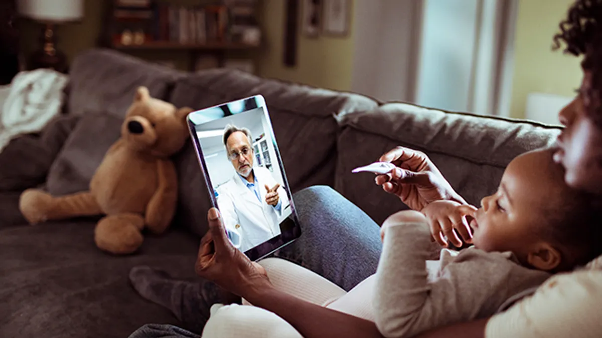 A baby sitting on a mom's lap on the couch. They are talking to a doctor on an i-pad.