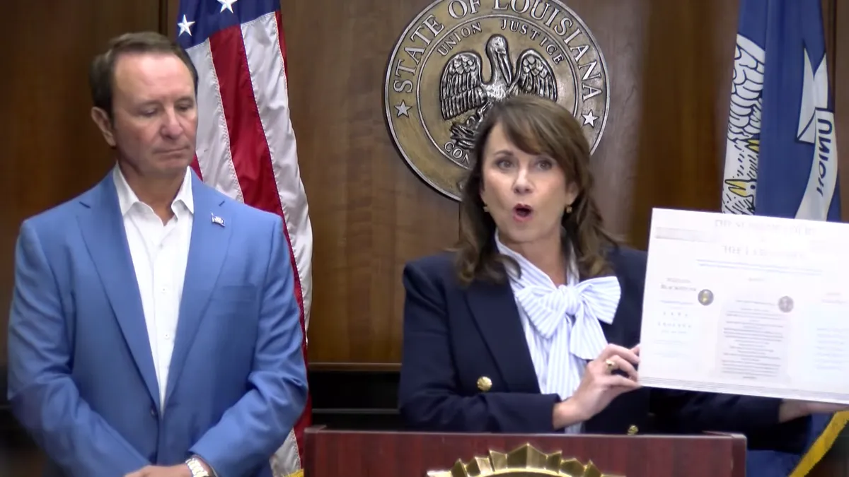 Attorney General Liz Murrill holds up a poster while standing behind a podium next to Gov. Jeff Landry