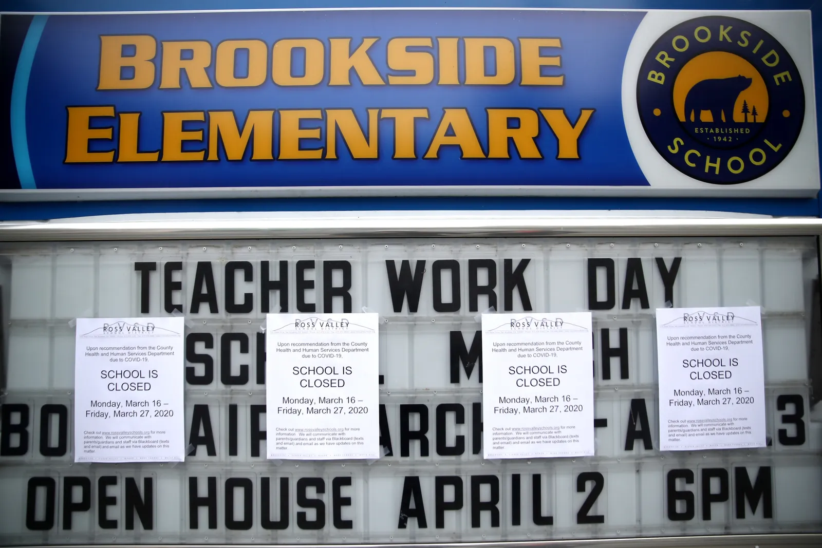 A marquee sign outside of a school has notes taped up saying school would be closed March 16-27, 2020