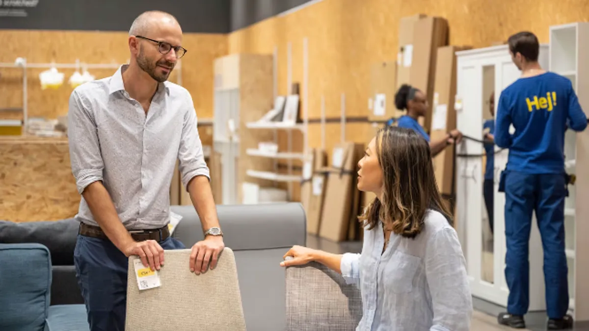 Two people talk to each other in an Ikea showroom surrounded by furniture products.