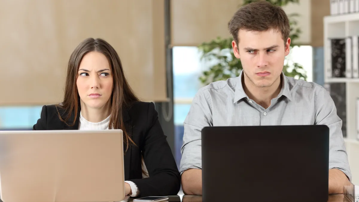 Two angry workers using computers next to each other