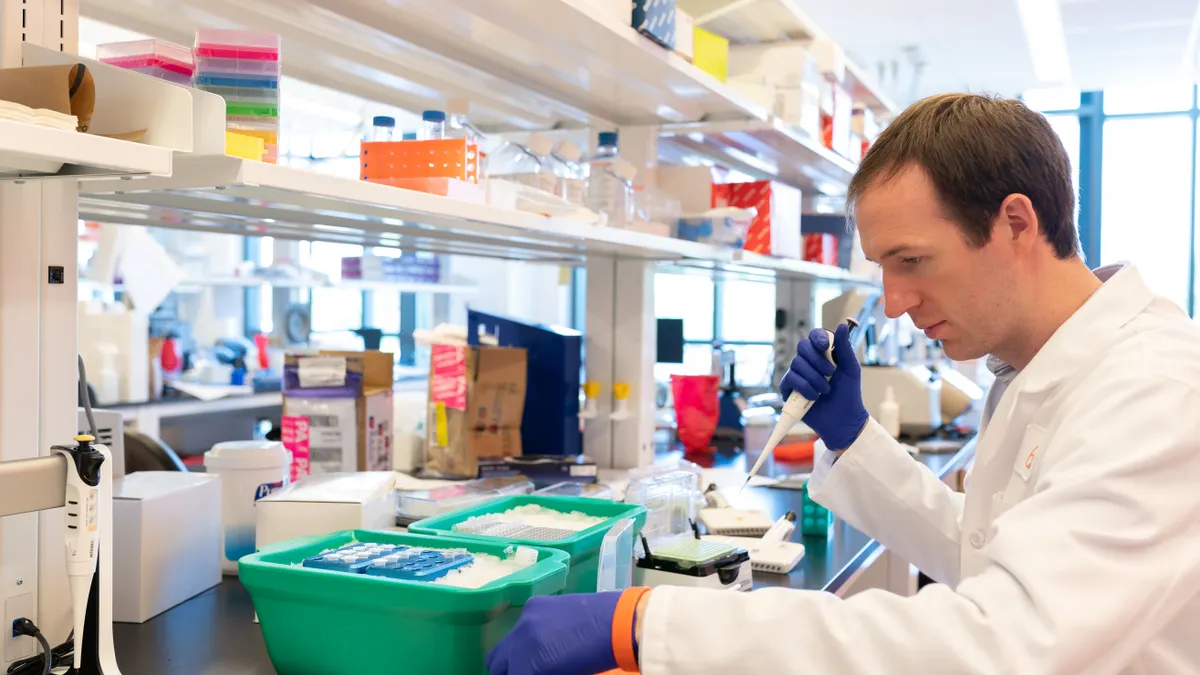 A person in a white lab coat and gloves works in a lab.