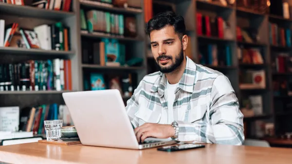 A man looks at his laptop in front of bookshelves.