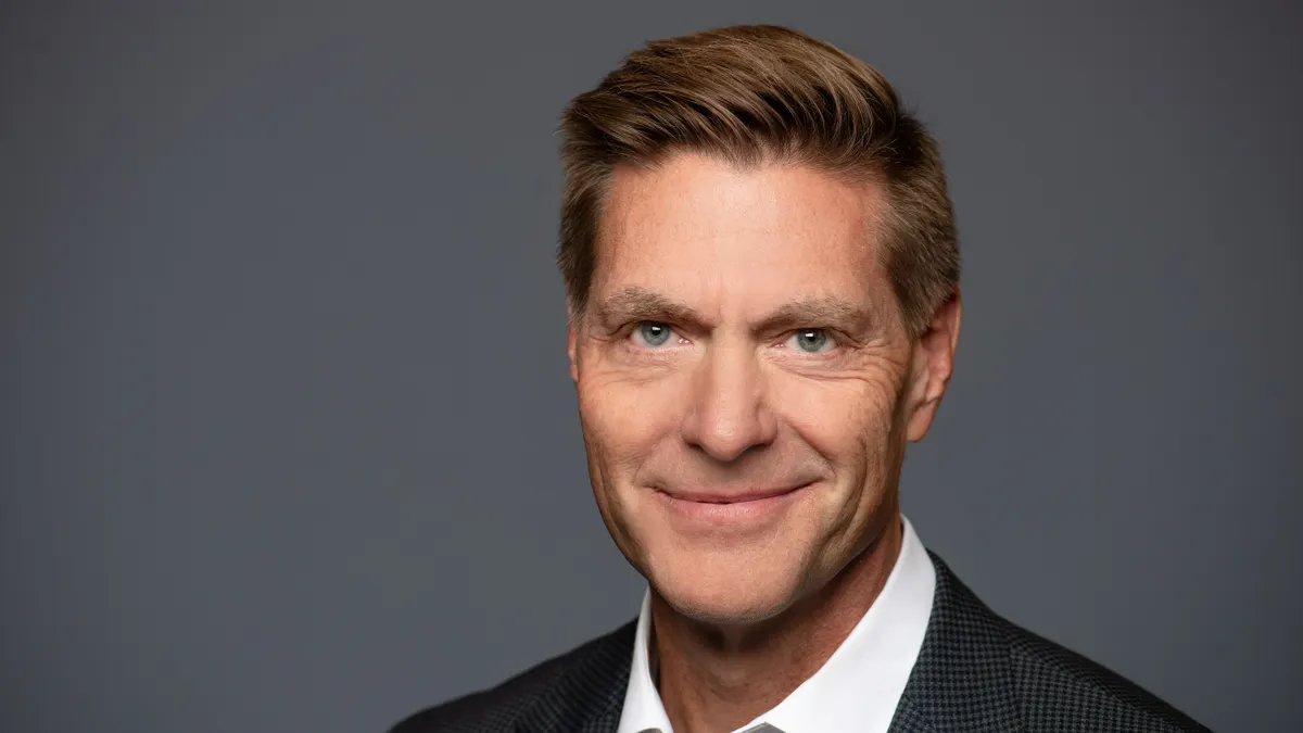 A headshot of Steve Nelson, wearing a grey suit against a grey background.