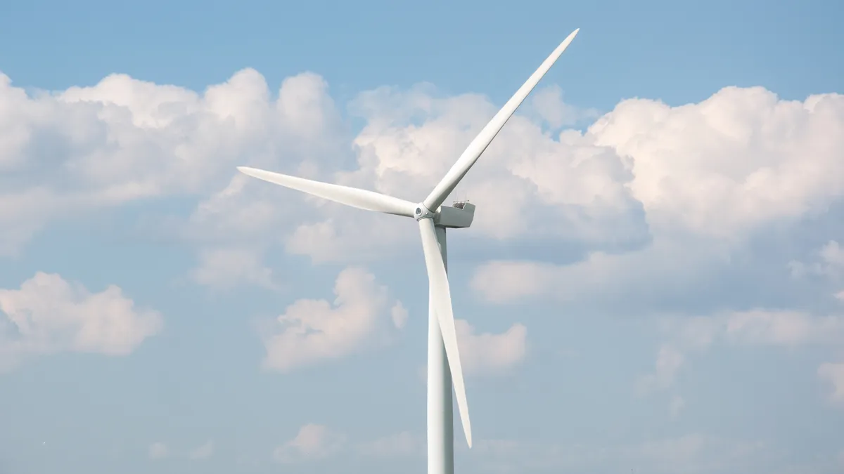 A wind turbine against a background of a blue sky and clouds.