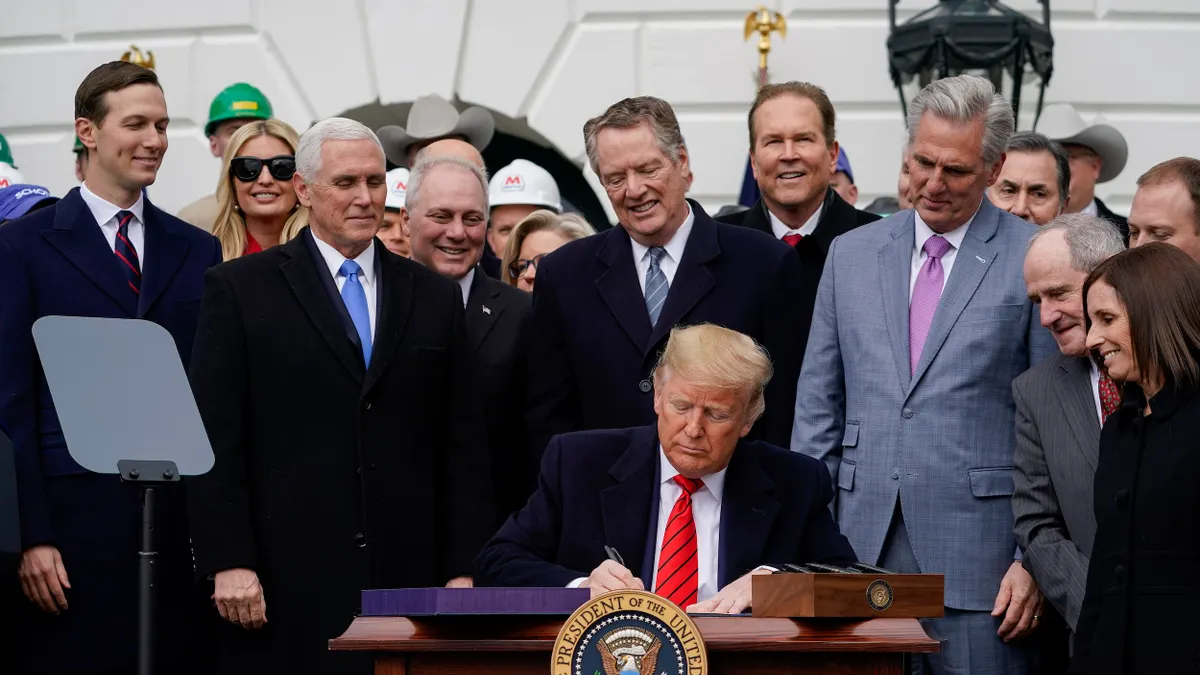 A crowd of people watches President Donald Trump sign a document