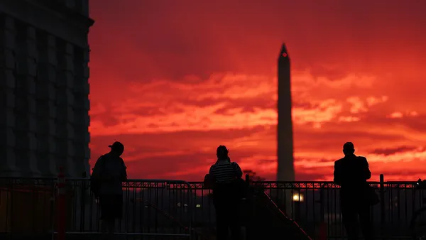 People are in the foreground looking toward the setting sun in the horizon and the Washington Monument.