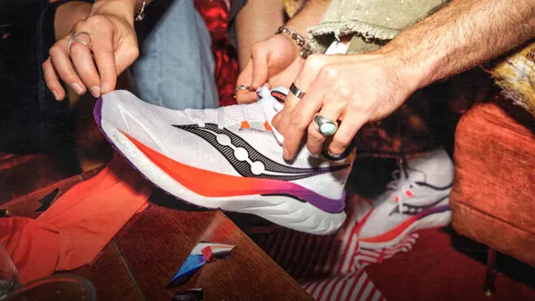 A person ties a sneaker with the word Saucony on it.