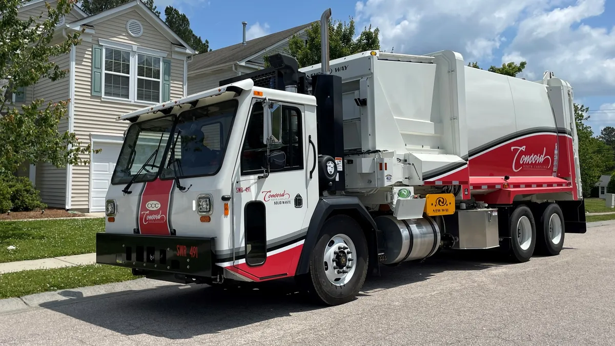 A white and red garbage truck labeled "Concord" parked in a residential neighborhood.