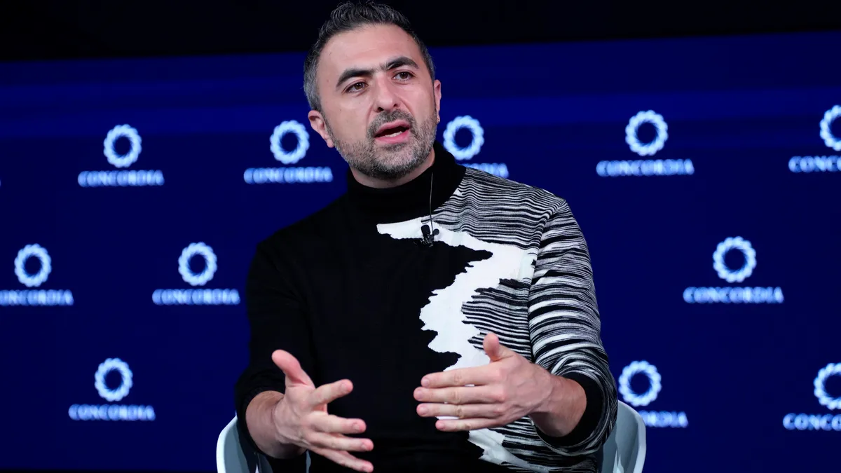 Mustafa Suleyman, wearing a black and white sweater, speaks during a tech conference