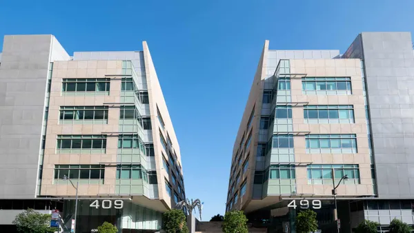 Two buildings stand parallel to each other on a street under a blue sky.