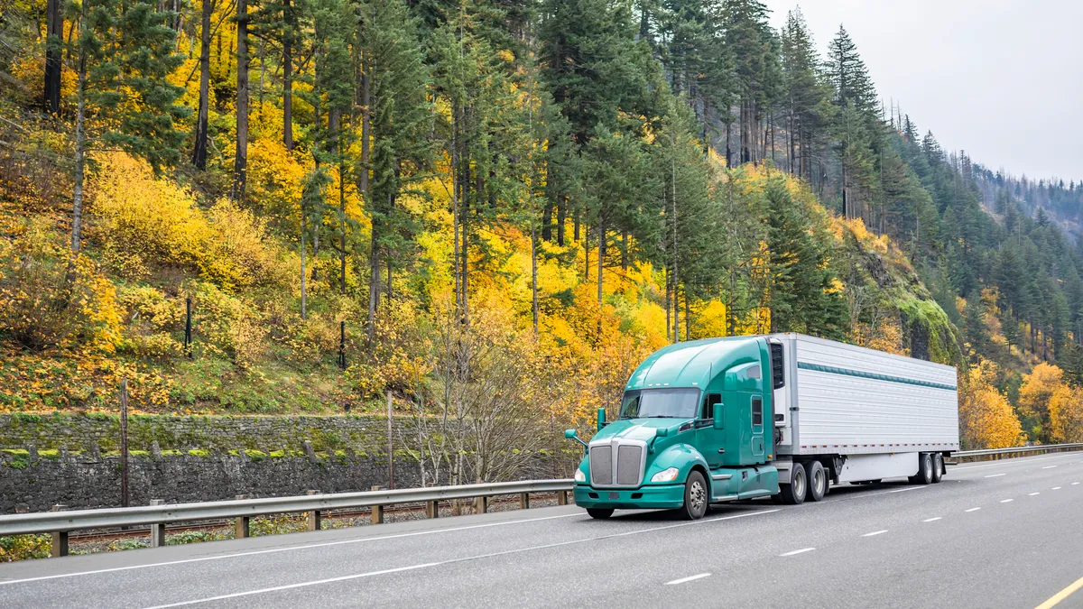 A reefer driving on highway road with autumn foliage on hills in the background.