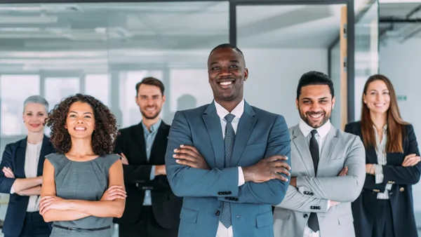 A diverse group of six lawyers stand near one another in an office setting