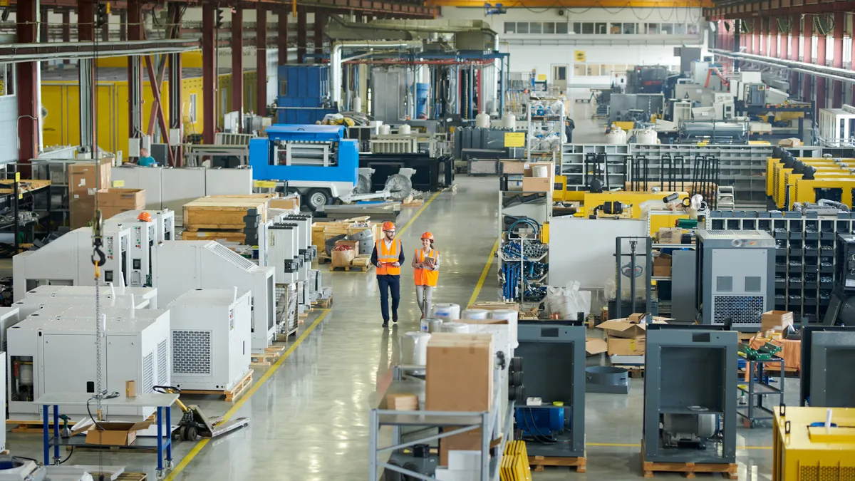 Two employees walk along the floor of a manufacturing plant and warehouse.