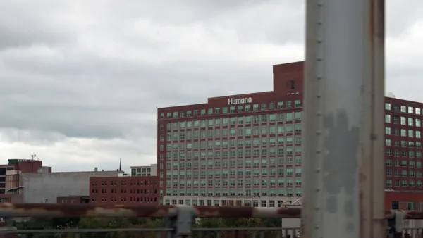 A red-brick mid-rise office building with rows of windows and a “Humana” sign on the roof, seen under a cloudy gray sky.