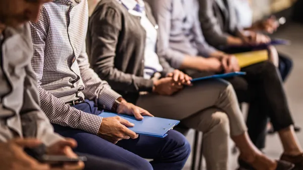 Large group of unrecognizable business people waiting for a job interview. Focus is on a person with blue clipboard.