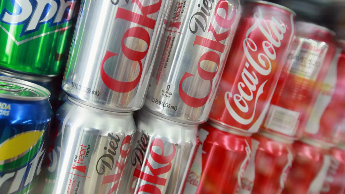 Cans of Sprite, Diet Coke and Coca-Cola are pictured on top of each other on a store shelf.
