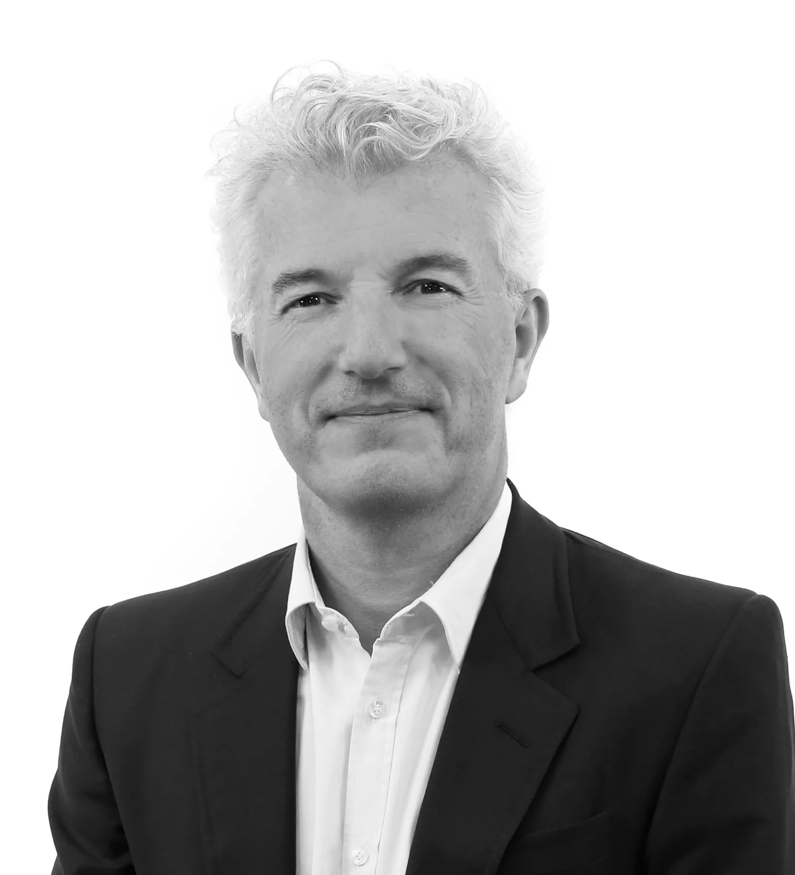 A person with short white hair wears a black jacket and white shirt in a corporate head shot.