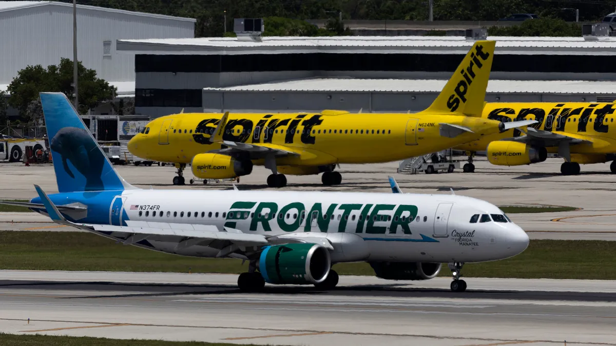 A plane with the Frontier logo taxies the runway in front of two planes with the Spirit logo.