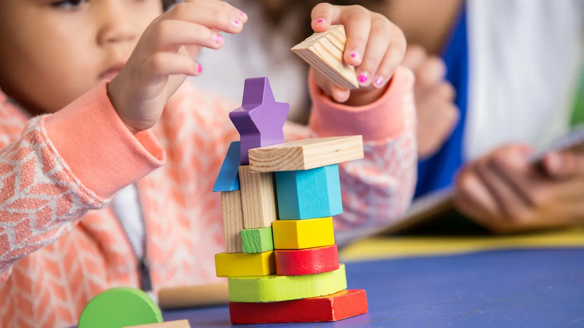 A toddler uses their hands to build blocks on a table in a classroom