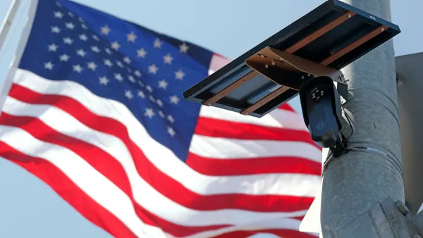 Camera attached to light pole with U.S. flag flying behind it.