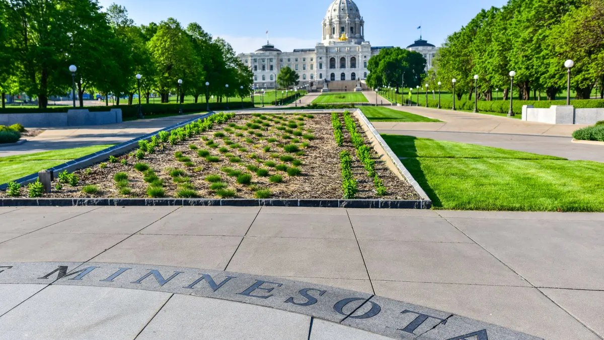A large white building with a dome in the center in the background, with green landscape in the front and "Minnesota" text on tiles.