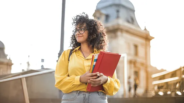 A student standing outside holding books and smiling