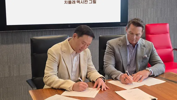 Two men in suits sign papers.