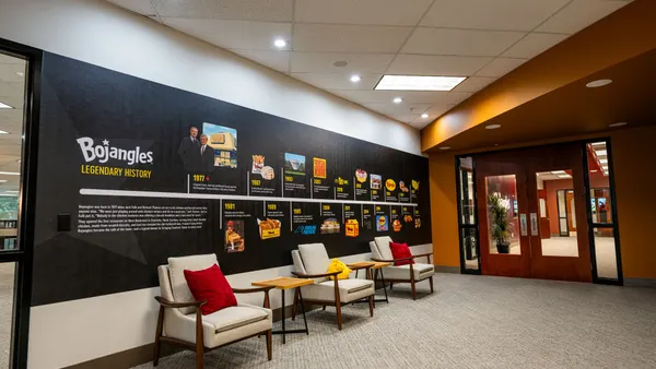 An image of a black wall inside an office with different dates on a timeline highlighting Bojangles history. In front of the wall there are three chairs.